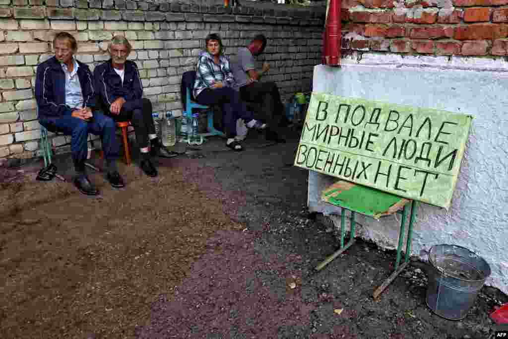 На этой фотографии, сделанной 16 августа 2024 года во время медиа-тура, организованного Украиной, изображены жители, сидящие рядом с табличкой &quot;В подвале гражданские, военных нет&quot; в подконтрольном Украине российском городе Суджа Курской области.&nbsp;